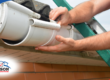Hands repairing a white plastic roof gutter.
